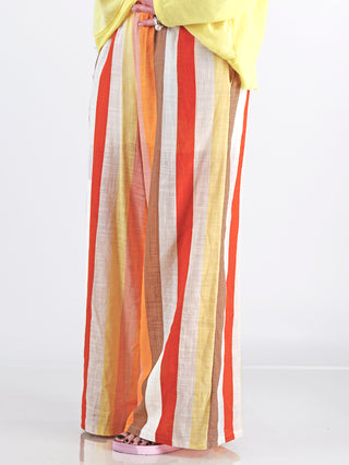 Frau trägt die OFF#DLY Leinenhose Duffy multicolor mit farbenfrohen Streifen, weites Bein und elastischem Bund, kombiniert mit sommerlichem Komfort und Stil.