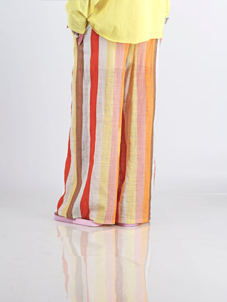 Person trägt die OFF#DLY Leinenhose Duffy multicolor mit farbenfrohen Streifen, weiten Beinen und elastischem Bund, kombiniert mit pinken Sandalen, ideal für sommerliche Anlässe.