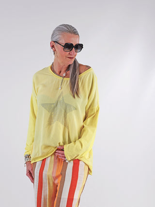 OFF#DLY Tee STAR yellow: Frau in gelbem Oversize-Shirt mit Stern-Print, grauem Haar, Sonnenbrille. Leichter Stoff, lässiger Schnitt, modisches Design. Perfekt für sommerliche Outfits und vielseitiges Styling.