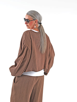 Frau mit langen Haaren und Sonnenbrille trägt die OFF#DLY Musselin Jacke Ritta mokka mit weiten Ärmeln und Spitzenborte, verleiht einen femininen, luftigen Look.