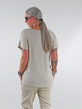 OFF#DLY Shirt Libella beige: Frau mit langen Haaren trägt ein beiges T-Shirt mit glitzernder Libellenapplikation und V-Ausschnitt, perfekt für lässige oder schicke Outfits.