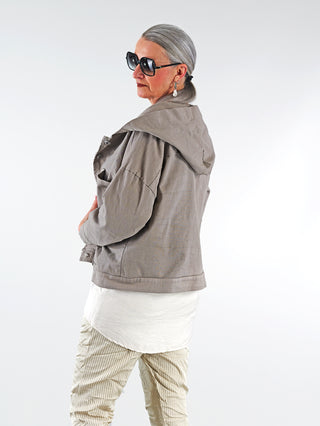 Frau trägt die OFF#DLY Jacke Zuleika taupe mit Kapuze und großen Taschen, dazu Sonnenbrille, präsentiert lässigen, modernen Look, passend für kühle Tage und Übergangszeit.