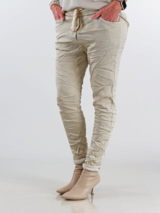 Beine einer Person in der OFF#DLY Pant Stripes Gitta beige, mit feinem Streifenmuster, lockerem Schnitt und schmal zulaufendem Bein, kombiniert mit tanfarbenen Stiefeln.