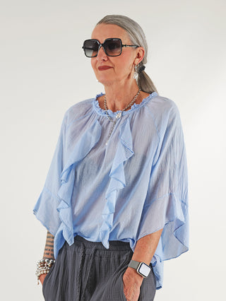 Frau trägt OFF#DLY Rüschen Bluse Frida lightblue, luftig mit Volants und 3/4-Ärmeln. Die Bluse hat einen runden Ausschnitt mit Rüschen, ideal für Sommer.