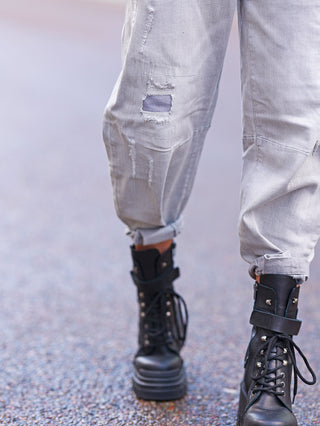 Eine Person trägt die OFF#DLY Relax Fit Destroy Denim lightgrey Jeans mit lässigem Schnitt und Destroyed-Details, kombiniert mit schwarzen Stiefeln für einen urbanen Look.