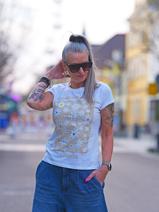 Frau mit Tätowierungen trägt das OFF#DLY Flower Market white/beige T-Shirt mit floralem Print und glänzenden Highlights, kombiniert mit Sonnenbrille. Perfekt für lässigen Frühlingslook.