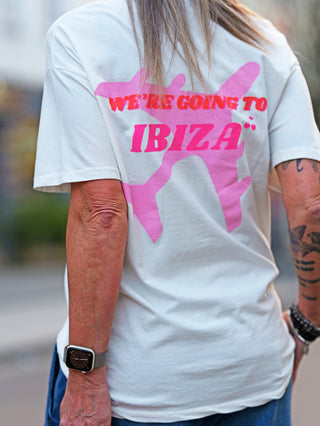 Person trägt das OFF#DLY Tee Ibiza creme, weißes T-Shirt mit pinkem IBIZA-Schriftzug vorne und großem Flugzeug-Print hinten, aus weichem Baumwoll-Elasthan-Mix, ideal für Sommerlook.