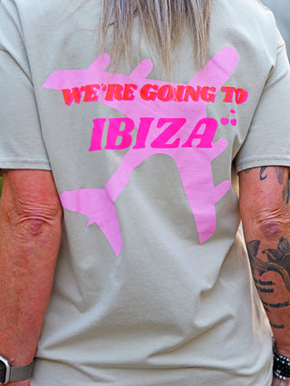 Person trägt ein OFF#DLY Tee Ibiza taupe mit pinkem IBIZA-Schriftzug auf der Vorderseite. Lockerer Schnitt, Rundhalsausschnitt, kurze Ärmel. Perfekt für sommerliche Freizeitlooks.