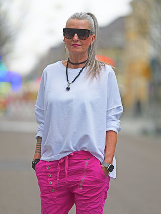 Eine Frau trägt den OFF#DLY Lightsweat Calista white, einen leichten Boxy-Sweater im Used-Look, kombiniert mit pinken Hosen und Sonnenbrille.
