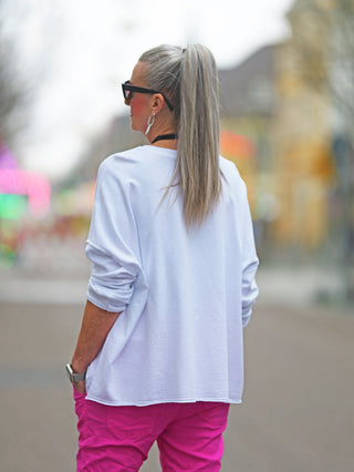 Frau trägt OFF#DLY Lightsweat Calista white, ein leichter Boxy-Sweater mit Used-Look, langen Ärmeln und Rundhalsausschnitt. Ideal für Übergangszeiten, bietet lockeren, lässigen Stil.