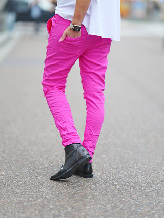 OFF#DLY Pant Celeste pink: Person trägt pinke Crinkle-Hose mit schwarzen Stiefeln, betont durch asymmetrischen Knopfverschluss und dekorative Reißverschlüsse für einen lässigen, modernen Look.