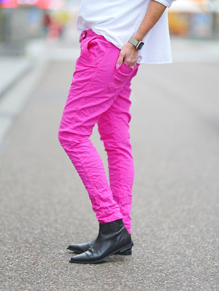 Person trägt OFF#DLY Hose Celeste pink mit schwarzen Stiefeln. Die Hose hat einen asymmetrischen Knopfverschluss und dekorative Reißverschlüsse, ideal für einen modernen, lässigen Look.