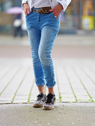 OFF#DLY Pant Indria lightblue zeigt eine Person in blauen Jeans mit Leopardenmuster-Schuhen und braunem Gürtel. Sichtbar sind Beine und Schuhe auf einer Betonfläche.