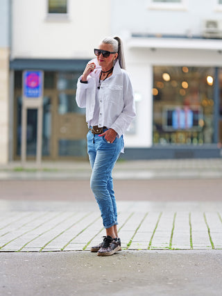 Frau auf dem Bürgersteig trägt OFF#DLY Pant Indria lightblue, Jogpant in Denim-Optik mit abnehmbarem Gürtel und Mini-Tasche, kombiniert mit Leopardenmuster-Schuhen, ideal für urbanen Alltags-Look.