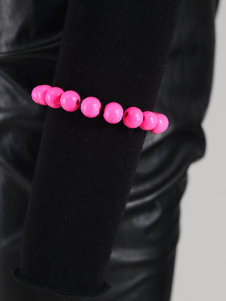 OFF#DLY Kugelarmband pink aus Holz mit runden, leichten Holzperlen auf einem elastischen Band, präsentiert auf schwarzem Stoff. Perfekt für sommerliche Outfits und als modisches Statement.