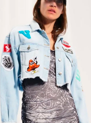 #VDR Denim Jacket iceblue: Frau trägt eine verkürzte Jeansjacke mit Fransen, auffälligen Patches und Stickereien. Vorderseite mit Knopfverschluss, Rückseite mit großem Peace-Patch und Be like no one!-Slogan.