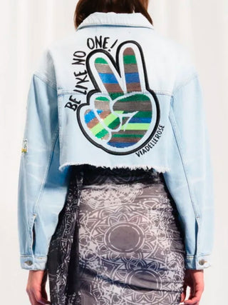 Person trägt #VDR Denim Jacket iceblue mit auffälligem Peace-Patch auf dem Rücken, verkürztem Schnitt und bunten Stickereien, vermittelt einen rebellischen, urbanen Stil.