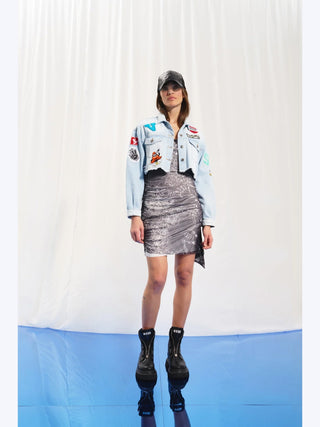 Frau trägt #VDR Denim Jacket iceblue mit ausgefranstem Saum und bunten Patches, darunter ein großer Peace-Patch auf dem Rücken. Kombiniert mit schwarzem Kleid und Boots.