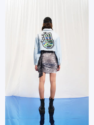 Frau trägt #VDR Denim Jacket iceblue mit ausgefranstem Saum, auffälligen Patches und Stickereien. Kombiniert mit schwarzem Hut und schwarzen Boots, zeigt ein rebellisches, urbanes Outfit.