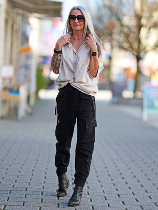 OFF#DLY Bluse Musselin Heart white beige, getragen von einer Frau auf dem Gehweg. Sie trägt schwarze Hosen und Sonnenbrillen, sichtbar sind Tattoos am Arm und die Bluse hat ein Herzmuster.