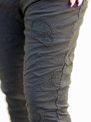 Nahaufnahme der OFF#DLY Pant Ava black, bestickte schwarze Crinkle-Hose mit feinem Paisley-Design und elastischem Bund, zeigt eleganten Boho-Stil und vielseitige Taschen.