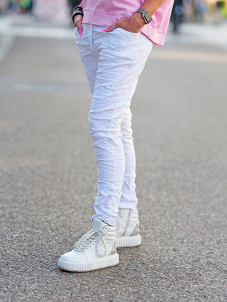 OFF#DLY Pant Ava white: Person trägt weiße bestickte Crinkle-Hose mit elastischem Bund und weißen Sneakers, betont durch Paisley-Design, ideal für sommerliche Looks.