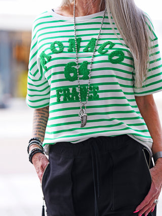 Damen-Sweatshirt OFF#DLY Ringelsweat Monaco white/green, grün-weiße Streifen, 3D-Schriftzug „MONACO 64 FRANCE“, lässiger Schnitt. Person trägt dazu schwarze Hose und pink lackierte Nägel.