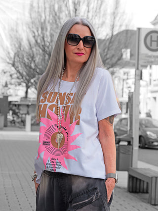 Frau trägt das OFF#DLY Tee Sunset white mit Retro-Schallplatten-Print und Rundhalsausschnitt, kombiniert mit Sonnenbrille, draußen in lässigem Stil. Perfekt für Sommerliebhaber.
