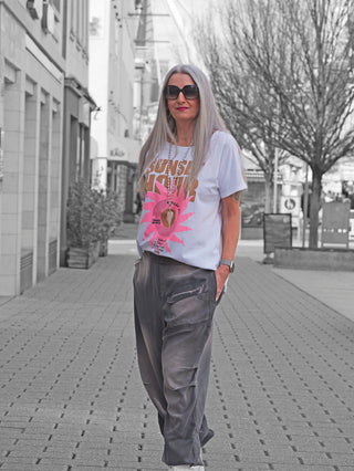 Frau trägt das OFF#DLY Tee Sunset white mit auffälligem Retro-Vinyl-Print, lockerer Schnitt, ideal zu Jeans. Perfekt für sommerliche Street-Fashion, fotografiert auf dem Bürgersteig.