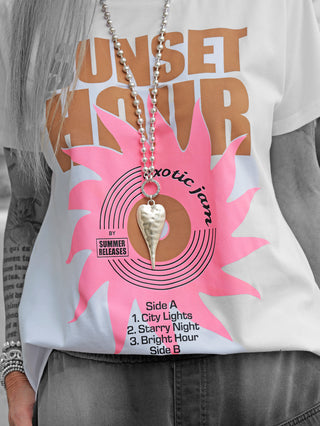 Eine Frau trägt das OFF#DLY Tee Sunset white mit einem Retro-Schallplatten-Print „Sunset Hour – exotic jam“ in Weiß, kombiniert mit einer goldenen Halskette.