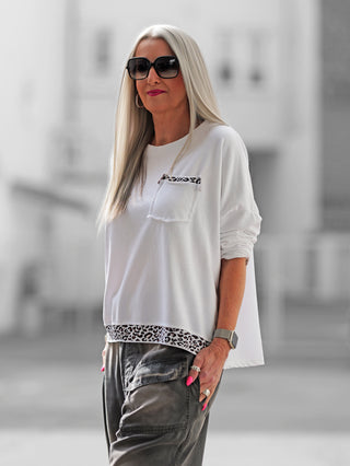 Eine Frau trägt den OFF#DLY Boxy Sweat Alba white/leo mit Oversize-Schnitt und Leo-Details an Saum und Tasche, kombiniert mit einer weißen Bluse und Sonnenbrille.