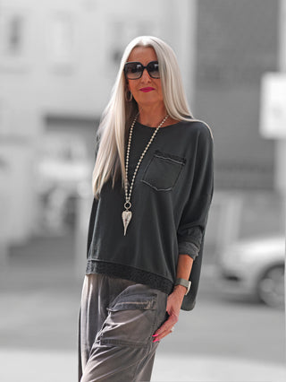 Frau trägt OFF#DLY Boxy Sweat Alba black/leo mit oversized Schnitt und Leo-Details an Saum und Brusttasche, kombiniert mit Sonnenbrille und Schmuck, lässiger Alltagslook.