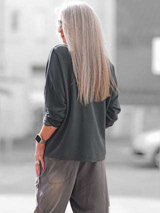 Frau mit langem Haar trägt OFF#DLY Boxy Sweat Alba black/leo, ein oversized Sweatshirt mit Leo-Details, sichtbarer Oversize-Schnitt und Brusttasche, ideal für trendige Alltagslooks.