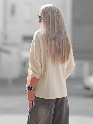 Frau mit langen Haaren trägt den OFF#DLY Boxy Sweat Alba vanille/leo, einen oversized Sweater mit Leodetails, Brusttasche und Uhr, perfekt für lässige Alltagslooks.