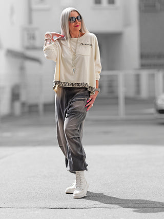 Frau trägt den OFF#DLY Boxy Sweat Alba vanille/leo, einen oversized Sweater mit Leo-Details am Saum und Brusttasche, perfekt kombiniert mit weißem Schuhwerk für einen modischen Streetwear-Look.