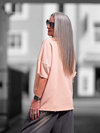 Frau mit grauen Haaren trägt Sonnenbrille und den OFF#DLY Sweat Lola apricot, ein oversize Kurzarmsweater mit Raw-Edge-Saum, der einen lässigen und modernen Look vermittelt.