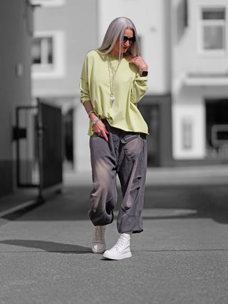 Eine Frau trägt den OFF#DLY Lightsweat Calista pistazie, einen leichten, boxy geschnittenen Sweater mit Used-Look, ideal für Übergangszeiten, aus weicher Baumwolle und Elasthan, perfekt für lässigen Stil.