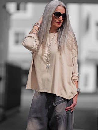 Frau trägt OFF#DLY Longsleeve Maelis beige, Oversize-Boxy-Schnitt, beige, mit Sonnenbrille, betont lässigen Stil und minimalistische Eleganz. Ideal für vielseitige, bequeme Looks.
