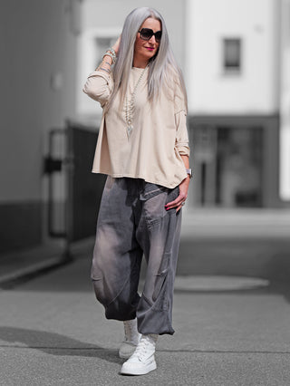 Frau trägt OFF#DLY Longsleeve Maelis beige, oversized, Boxy Fit, mit langen Ärmeln und rundem Ausschnitt, kombiniert mit Sonnenbrille und grauer Hose, für einen lässigen Look.