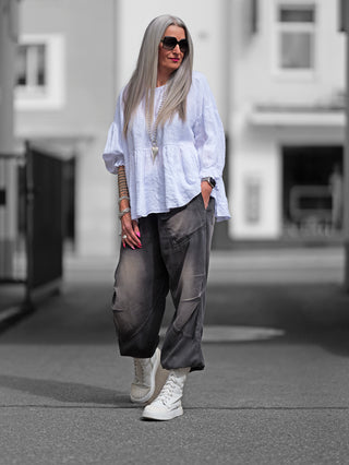 OFF#DLY Leinenshirt Wilma getragen von einer Frau mit langen Haaren, Sonnenbrille und weißen High-Top-Sneakers. Das luftige Leinenmaterial und die femininen Volants sind deutlich sichtbar.