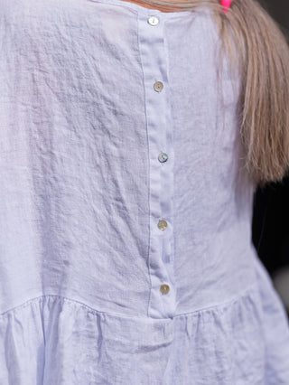 Nahaufnahme des OFF#DLY Leinenshirt Wilma, einer weißen Bluse aus 100% Leinen mit Volants, Rundhalsausschnitt und gerafften Ärmeln, die einen femininen und luftigen Sommerlook bietet.