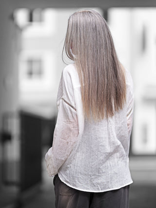 Frau trägt die OFF#DLY Bluse Viola white, eine weiße, leichte Oversize-Bluse mit Hohlsaum-Details, langen Ärmeln und entspannter Silhouette, ideal für warme Tage.