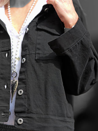 OFF#DLY Jacke Tiana schwarz: Eine Person trägt eine schwarze Jacke mit markanten Druckknöpfen und aufgesetzten Brusttaschen im Oversized Denim-Stil, passend bis Größe 42.