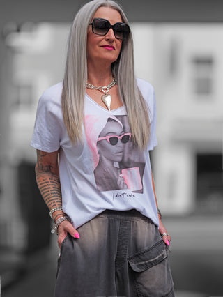Frau trägt OFF#DLY Tee Valencia white/pink mit „I don't care“ Slogan, Sonnenbrille, und V-Ausschnitt. Das Shirt ist locker geschnitten und aus weicher Baumwolle.