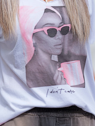 Person trägt OFF#DLY Tee Valencia weiß/pink mit Fotoprint einer Frau mit Sonnenbrille und pinker Tasse, V-Ausschnitt, lässiger Schnitt, perfekt für einen modischen Statement-Look.