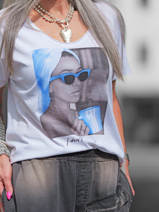 Frau trägt das OFF#DLY Tee Valencia white/blue mit V-Ausschnitt und auffälligem Fotoprint einer Frau mit Sonnenbrille, begleitet von farbigen Akzenten. Perfekt für lässige, modische Statements.