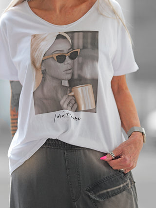 Frau trägt das OFF#DLY Tee Valencia white/beige mit V-Ausschnitt und Fotoprint einer Frau mit Sonnenbrille, Handtuch und Tasse. Statement-Slogan „I don't care“ sichtbar.