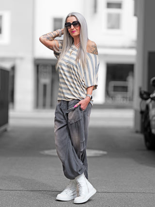 Eine Frau trägt das OFF#DLY Ringel Shirt Sienna taupe/beige mit grauen und beigen Streifen, lockerem Schnitt und kurzen Ärmeln, posiert lässig für ein Foto.