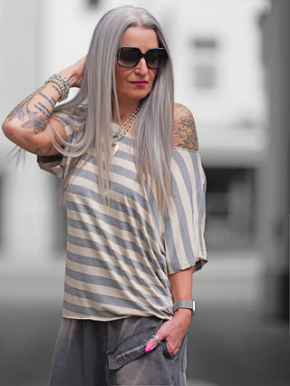 Frau trägt das OFF#DLY Ringel Shirt Sienna taupe/beige, ein locker gestreiftes Shirt mit Rundhalsausschnitt und kurzen Ärmeln, kombiniert mit Tattoos und Sonnenbrille.