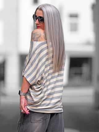 Frau trägt das OFF#DLY Ringel Shirt Sienna taupe/beige mit grauen Streifen, kurzen Ärmeln und lockerem Schnitt. Sichtbar ist ein Schultertattoo und Sonnenbrille.
